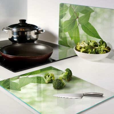 Glas-Schneidebrett mit Blattmotiv vor verschwommenem grünen Hintergrund