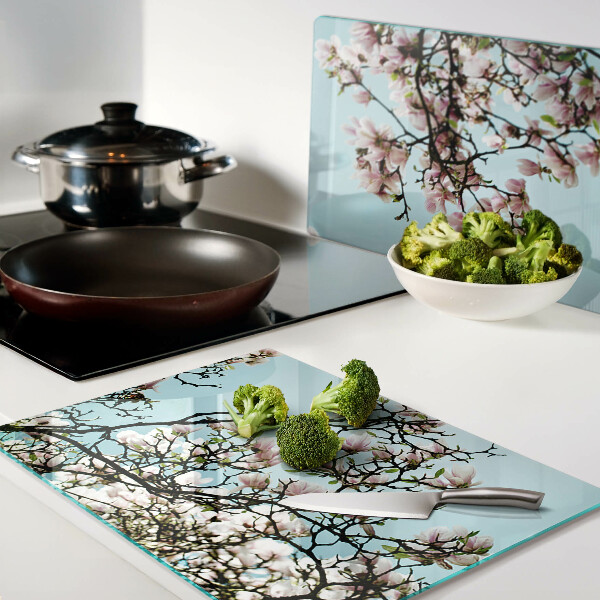 Glas-Schneidebrett mit Magnolienblüten auf blauem Hintergrund