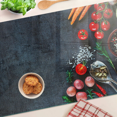 Glas-Schneidebrett mit Motiv von Gemüse und Gewürzen auf dunklem Hintergrund