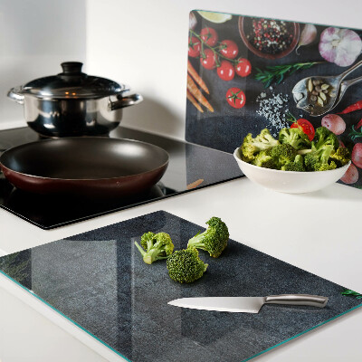 Glas-Schneidebrett mit Motiv von Gemüse und Gewürzen auf dunklem Hintergrund