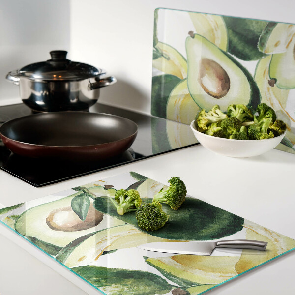 Glas-Schneidebrett mit Avocado-Motiv und Blättern im Hintergrund
